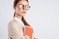 Beautiful young woman with glasses holds a notebook against a light background, portrait, teacher