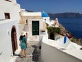 Beautiful young woman in green dotted dress walking in Oia, Santorini streets. White houses, blue sea