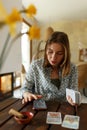 Beautiful young woman is guessing on cards with tarot, runes on wooden table and uses an online app in phone to