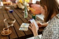 Beautiful young woman is guessing on cards with tarot, runes on wooden table and uses an online app in phone to