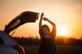 Beautiful young woman happy and dancing in a car`s trunk during a road trip in Europe in the last minutes of Golden Hour Royalty Free Stock Photo