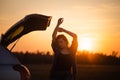 Beautiful young woman happy and dancing in a car`s trunk during a road trip in Europe in the last minutes of Golden Hour Royalty Free Stock Photo