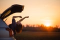 Beautiful young woman happy and dancing in a car`s trunk during a road trip in Europe in the last minutes of Golden Hour Royalty Free Stock Photo