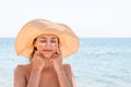 Beautiful young woman in hat is applying sunblock under her eyes and on her nose like Indian. Sun protection concept Royalty Free Stock Photo