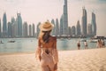Beautiful young woman in a hat on the background of the Dubai Marina. A beautiful woman rear view walking on the beach in Dubai.