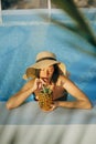 Beautiful young woman in hat drinking delicious cocktail from pineapple and relaxing in pool, summer vacation. Girl enjoying warm Royalty Free Stock Photo