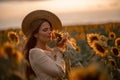 Beautiful young woman in a hat enjoying nature on a field of sunflowers at sunset. Summer. Attractive brunette with long Royalty Free Stock Photo