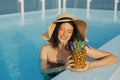 Beautiful young woman in hat holding  cocktail in pineapple and relaxing in pool, summer vacation. Girl enjoying warm sunshine, Royalty Free Stock Photo