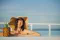 Beautiful young woman in hat relaxing in pool with delicious cocktail in pineapple. Summer vacation. Girl enjoying warm sunshine Royalty Free Stock Photo