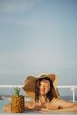 Beautiful young woman in hat relaxing in pool with delicious cocktail in pineapple. Summer vacation. Girl enjoying warm sunshine Royalty Free Stock Photo