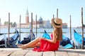 Beautiful young woman with hat sitting on the edge of Venetian Lagoon looking at stunning panoramic view of Venice, Italy Royalty Free Stock Photo