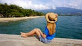 Beautiful young woman with hat sitting on pier looking at panoramic view of Ilhabela Island, Brazil Royalty Free Stock Photo