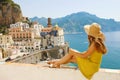 Beautiful young woman with hat sitting on wall looking at stunning panoramic village of Atrani on Amalfi Coast, Italy Royalty Free Stock Photo