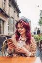 Beautiful young woman having coffee in outdoor cafe while using smartphone. Portrait of stylish girl Royalty Free Stock Photo