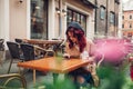 Beautiful young woman having coffee in outdoor cafe while using smartphone. Portrait of stylish girl Royalty Free Stock Photo