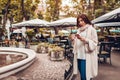 Beautiful young woman having coffee by outdoor cafe while using smartphone. Portrait of stylish girl typing message Royalty Free Stock Photo