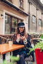 Beautiful young woman having coffee in outdoor cafe while using smartphone. Portrait of stylish girl typing message Royalty Free Stock Photo