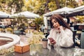 Beautiful young woman having coffee in outdoor cafe while using smartphone. Portrait of stylish girl typing message Royalty Free Stock Photo