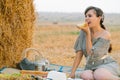 Beautiful young woman having a picnic and eats some bread near a hay bale in the middle of a wheat field in summer Royalty Free Stock Photo