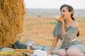 Beautiful young woman having a picnic and eats some bread near a hay bale in the middle of a wheat field in summer Royalty Free Stock Photo