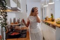 Beautiful young woman in headphones listening to music in kitchen. Frying pancakes.