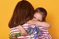 Beautiful young woman and her charming little daughter hugging indoor. Child congratulates mom with Mother`s Day, gives flowers, Royalty Free Stock Photo