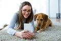 Beautiful young woman with her dog using mobile phone at home.