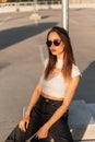 Beautiful young woman hipster in vintage sunglasses in cool black baseball cap in youth casual summer clothes rest on asphalt in Royalty Free Stock Photo