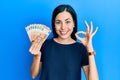 Beautiful young woman holding bunch of 50 euro banknotes smiling positive doing ok sign with hand and fingers Royalty Free Stock Photo
