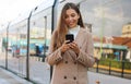Beautiful young woman holding cellular updating information about city transport online. Smiling business woman satisfied with