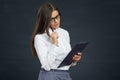 Beautiful young woman holding clipboard with pen thinking. Royalty Free Stock Photo