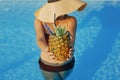 Beautiful young woman holding cocktail in pineapple and relaxing in pool, summer vacation. Girl in hat enjoying warm sunshine, Royalty Free Stock Photo