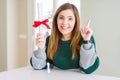 Beautiful young woman holding degree with red bow surprised with an idea or question pointing finger with happy face, number one Royalty Free Stock Photo