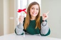 Beautiful young woman holding degree with red bow very happy pointing with hand and finger to the side Royalty Free Stock Photo