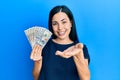 Beautiful young woman holding dollars smiling cheerful offering palm hand giving assistance and acceptance Royalty Free Stock Photo