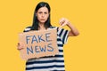 Beautiful young woman holding fake news banner with angry face, negative sign showing dislike with thumbs down, rejection concept