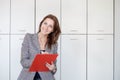 Beautiful young women is holding a folder, looking at camera and smiling while standing in office Royalty Free Stock Photo