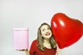 Beautiful young woman holding heart shape air balloon and gift box on a grey background.