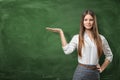 Beautiful young woman holding her open palm and showing at the empty area on the green chalkboard behind her Royalty Free Stock Photo