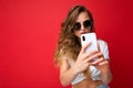 beautiful young woman holding mobile phone taking selfie photo using smartphone camera wearing everyday stylish outfit Royalty Free Stock Photo