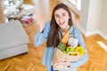 Beautiful young woman holding paper bag full of healthy groceries very happy and excited, winner expression celebrating victory Royalty Free Stock Photo