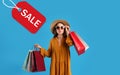 Beautiful young woman holding paper shopping bags and tag with word SALE on light blue background Royalty Free Stock Photo