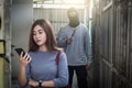 Beautiful young woman holding smartphone and being stalked by man criminal with the knife Royalty Free Stock Photo