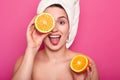 Beautiful young woman holds half of orange in her hand and covers eye with another part of fruit. Attractive lady with towel on Royalty Free Stock Photo