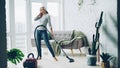 Beautiful woman is hoovering the floor at home using modern vacuum cleaner and listening to music with headphones Royalty Free Stock Photo