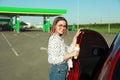 Beautiful young woman with hot dog opening car door at gas station. Space for text Royalty Free Stock Photo