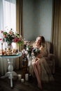 Beautiful young woman in a house dress in the boudoir, decorated with beautiful flowers, sitting on a white bed with a canopy, fas Royalty Free Stock Photo