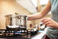 Beautiful young woman housewife prepairing dinner, hold in hands big steel saucepan, standing it on gas-stove. Royalty Free Stock Photo