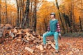 A beautiful young woman in jeans and a jacket, posing with an axe in her hands near the logs. Autumn forest in the background