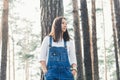 Beautiful young woman in jeans overalls standing in woodland